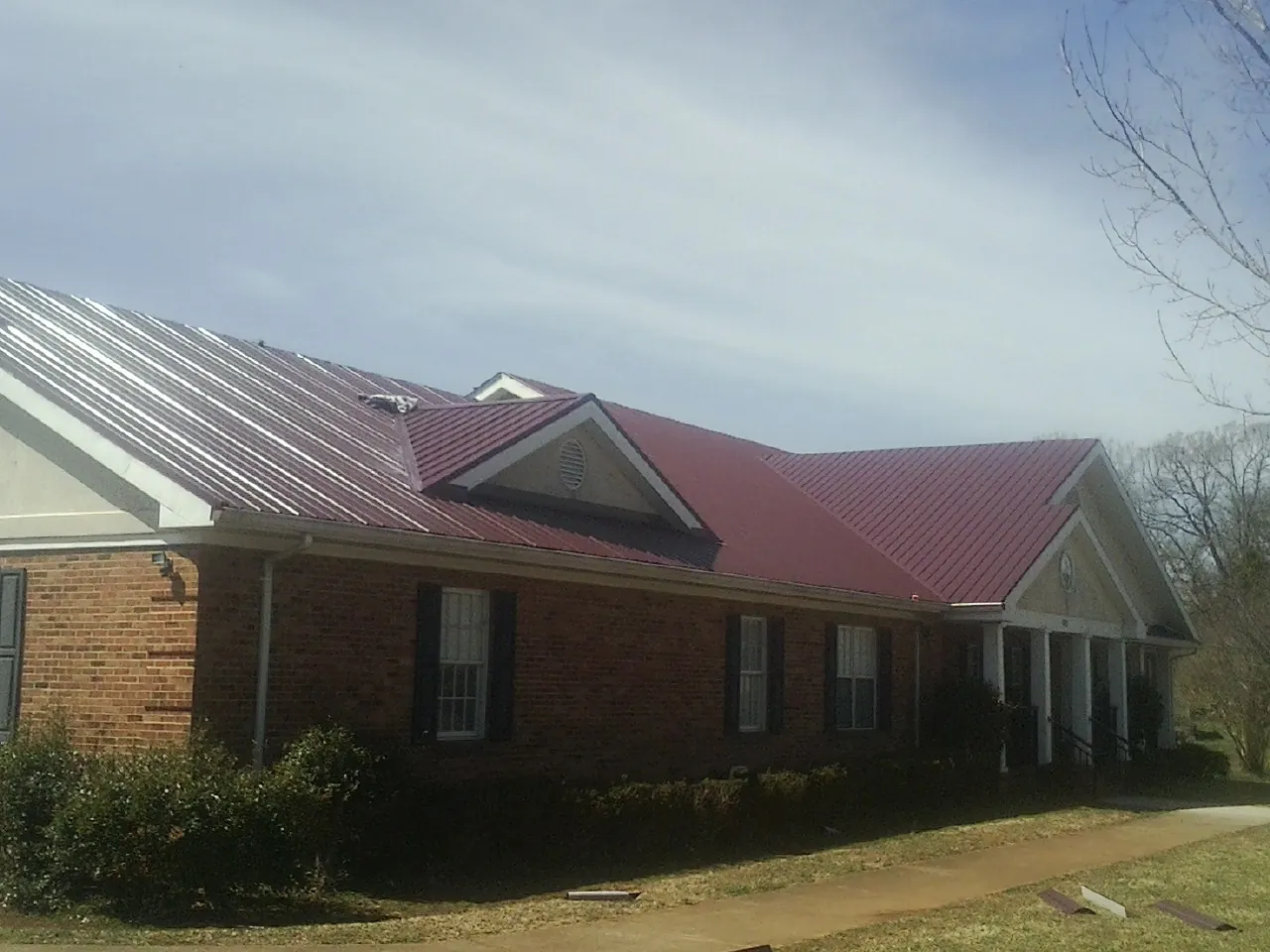 Red metal roof with gabled entries on a long brick building, from a Hail Damage Roof Repair job in Umpqua