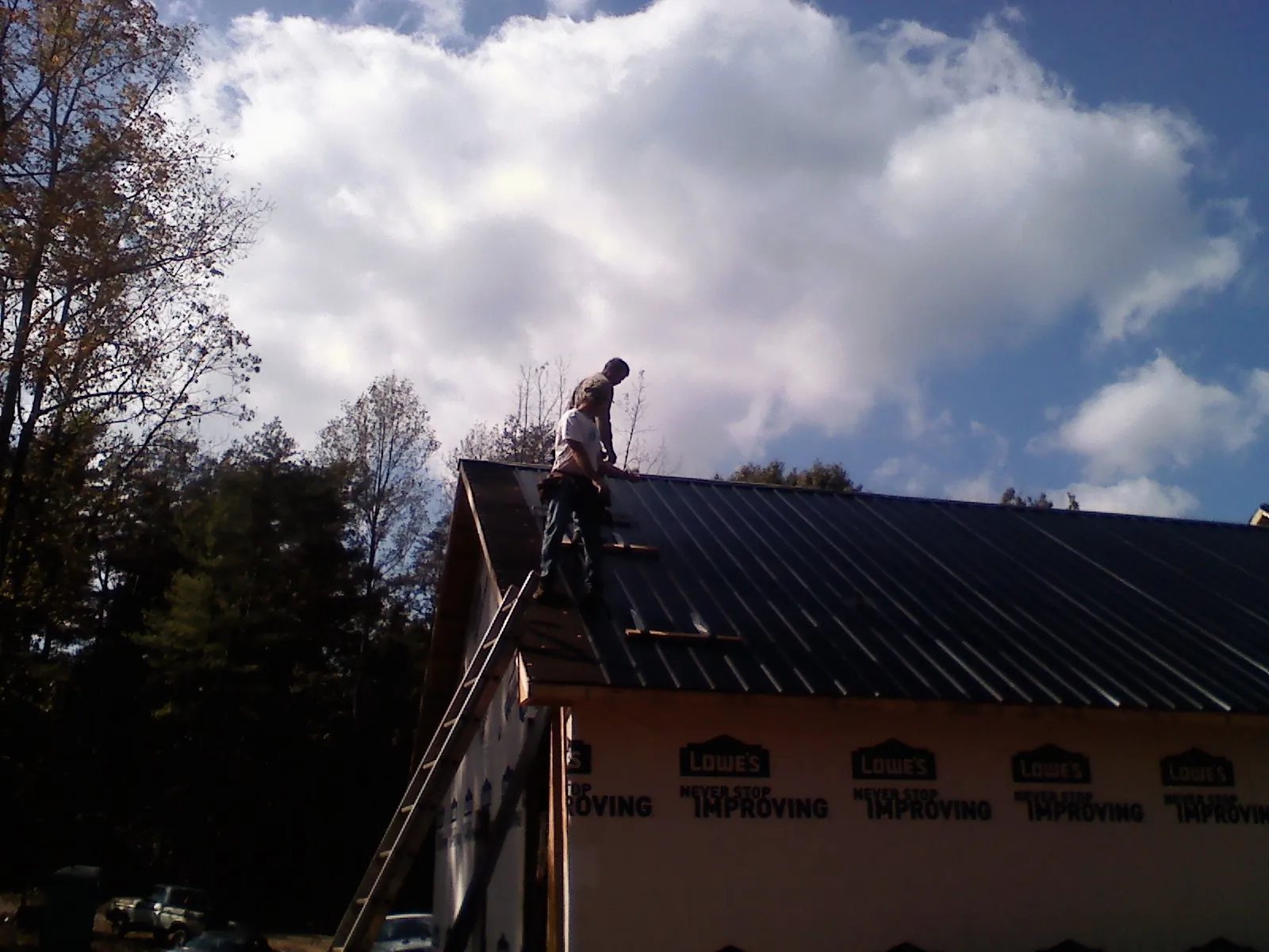 Roofer fastening dark metal panels high against a cloudy sky, from a Roof Inspection job in Umpqua