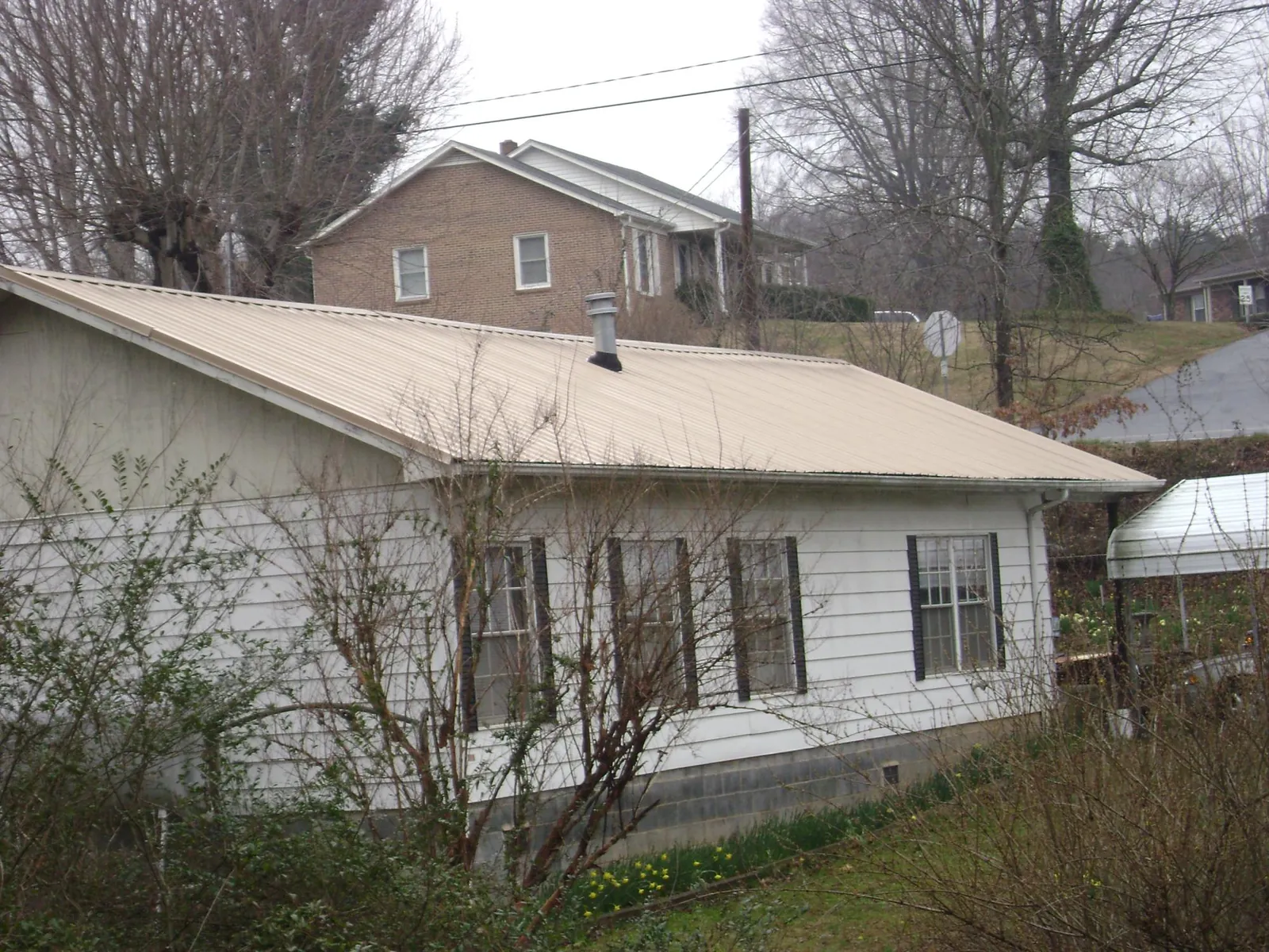 Tan metal roof on a white sided house set into a hillside — Commercial Roofing by Roofing Brothers in Umpqua